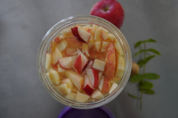Manzanas rojas troceadas en kefir de agua en un tarro de cristal Kefirko, con una manzana entera y hierba verde cerca.
