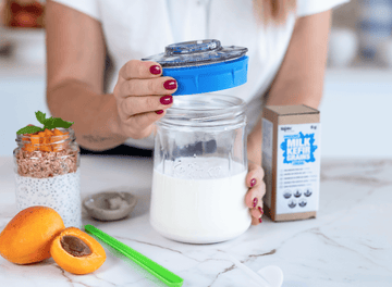 Manos colocando una tapa azul en un tarro de vidrio con leche para preparar kéfir casero.