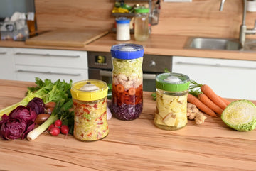 Tres tarros de vidrio con vegetales en capas listos para la fermentación en una encimera de cocina.