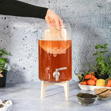 tarro de cristal con combucha y mano extrayendo el scoby de kombucha