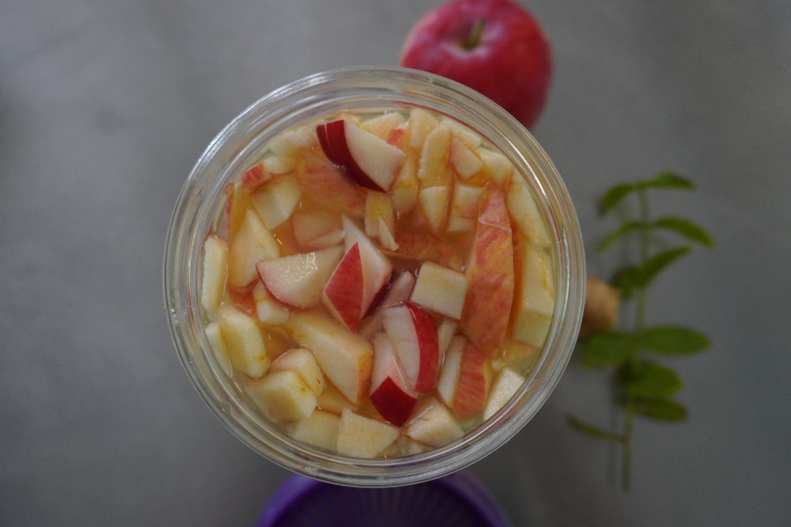 Manzanas rojas troceadas en kefir de agua en un tarro de cristal Kefirko, con una manzana entera y hierba verde cerca.