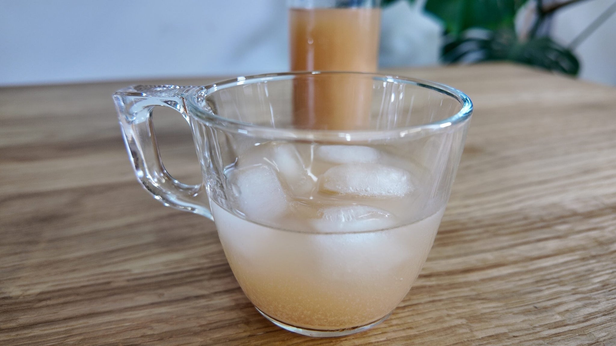 Primer plano de una taza de vidrio con una bebida probiótica de jengibre y kombucha con hielo sobre una superficie de madera.
