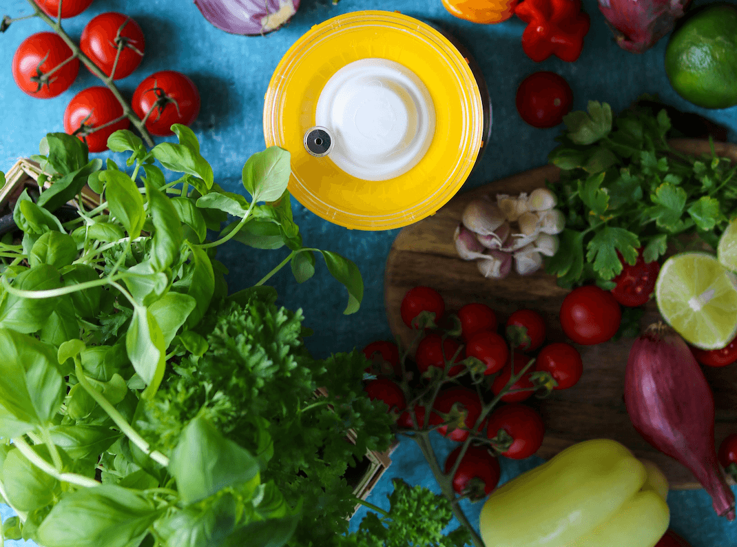 Vista cenital de un tarro de fermentación rodeado de verduras de primavera frescas como tomates, hierbas y cebollas.