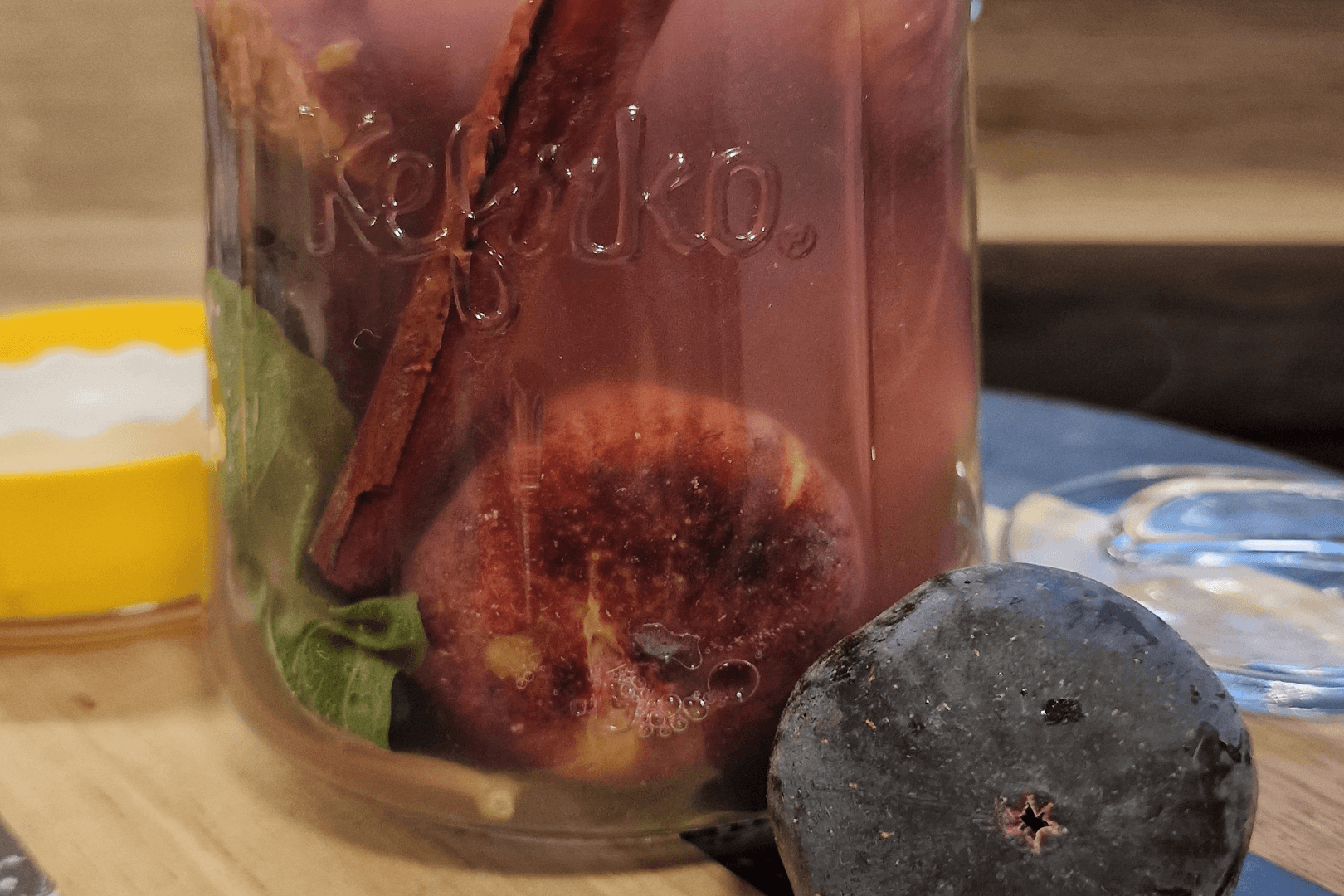 Un tarro de cristal Kefirko contiene higos, albahaca y canela junto a un higo sobre una superficie de madera.