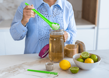 Una persona añade gránulos de kéfir con una cuchara verde a un tarro de vidrio para iniciar la fermentación.