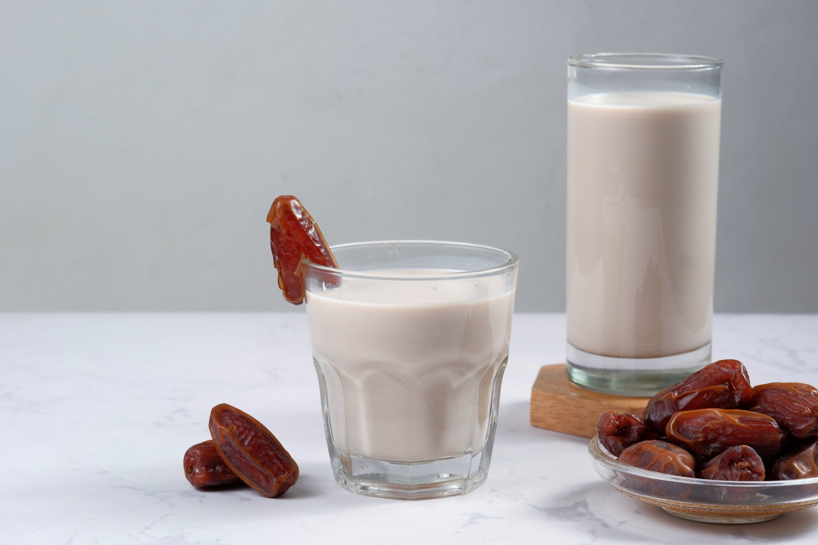 Dos vasos de kéfir de leche sobre una mesa de mármol, con un plato de dátiles y uno decorando el borde del vaso.