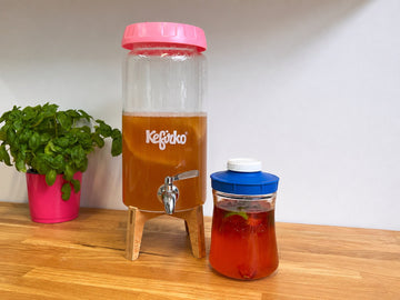Kombucha de fresa embotellada junto a fresas frescas, hinojo y hojas de albahaca