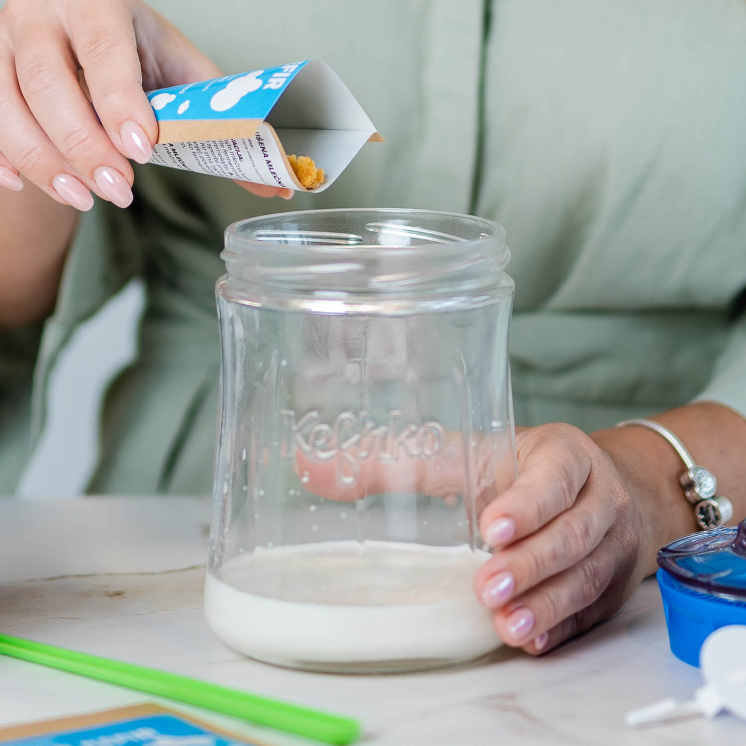 Manos vierten gránulos de un sobre en un tarro de vidrio Kefirko con leche, el primer paso de cómo hacer kéfir.