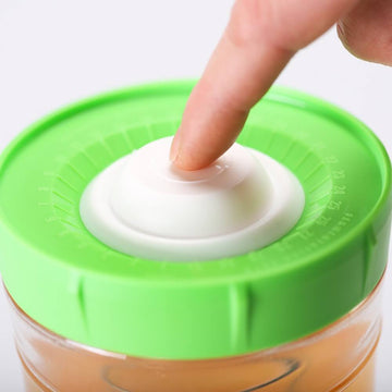 Dedo presionando la bomba de aire en la tapa verde de un tarro de fermentación para extraer el oxígeno.