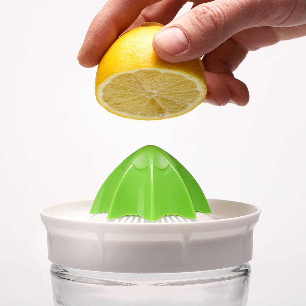 Una mano sostiene medio limón sobre un exprimidor de cítricos verde colocado sobre un tarro de cristal Kefirko