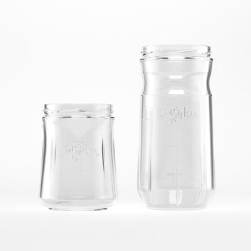 Dos tarros vacíos de Kefirko tarro de cristal de diferentes alturas están uno al lado del otro sobre un fondo blanco.