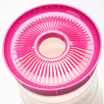 Vista superior de una tapa de colador Kefirko rosa con secciones de agua y leche etiquetadas en un fermentador transparente.