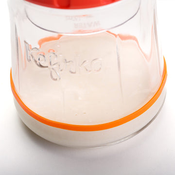 Primer plano del fondo de un tarro de vidrio Kefirko mostrando un cultivo de masa madre con una banda naranja en la base.