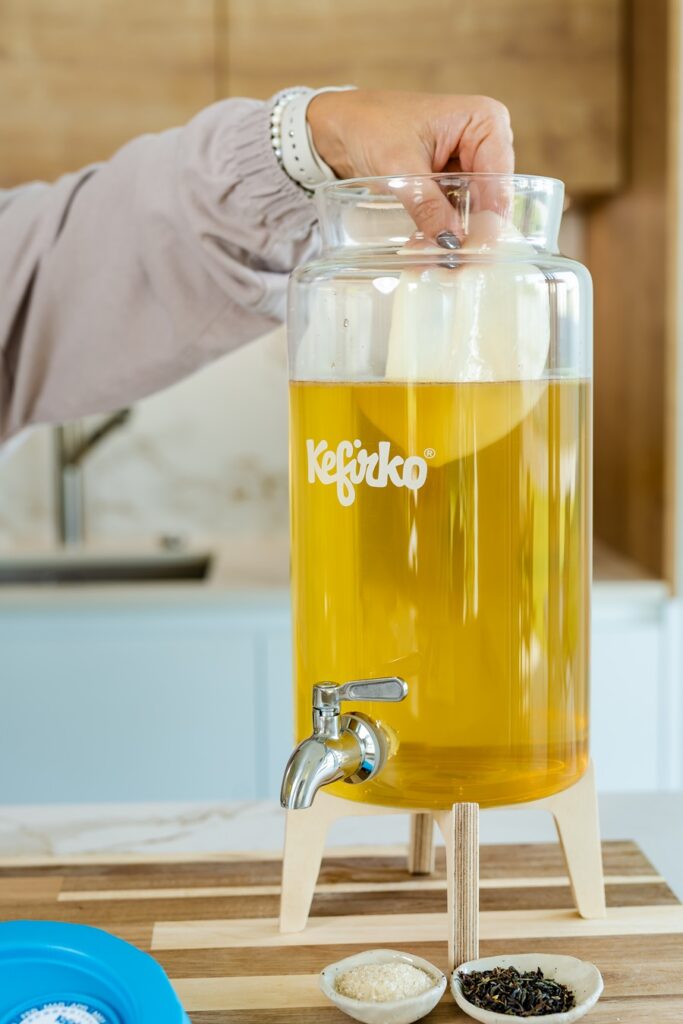 Mano introduciendo una kombucha madre en un fermentador de vidrio Kefirko con té para iniciar la fermentación.