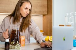Mujer siguiendo instrucciones en un portátil para hacer kombucha, con una jarra de té oscuro al lado.