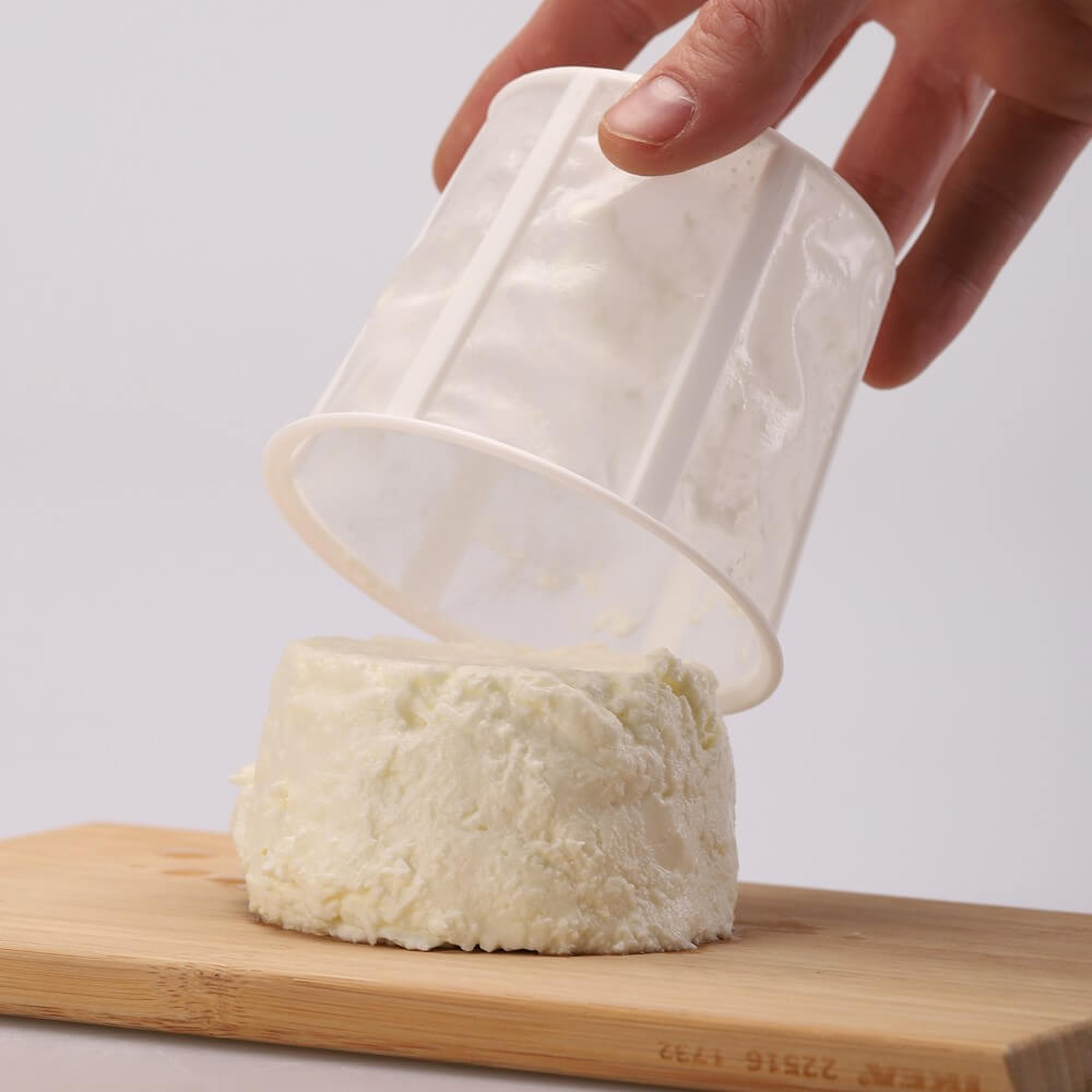 Primer plano de un queso fresco perfectamente moldeado con el cestillo del fermentador de queso de Kéfir Kefirko sobre una tabla de madera.