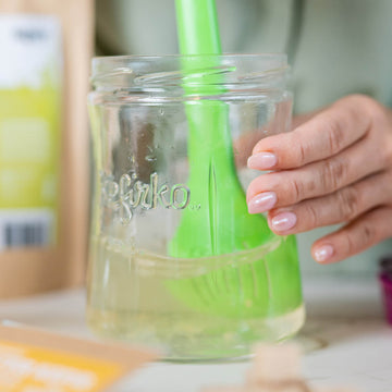 Persona removiendo líquido en un tarro de vidrio Kefirko, un paso clave en la fermentación casera.