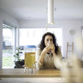 Una persona está sentada en la encimera de la cocina, sosteniendo y bebiendo de un vaso. Hay un dispensador de bebidas grande con la etiqueta 