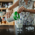 mujer colando kefir de leche en vaso sobre encimera de la cocina